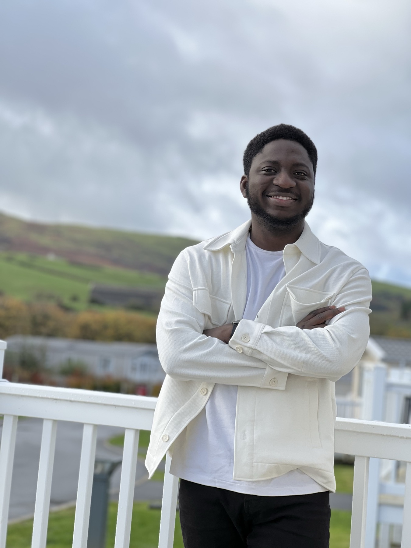 Michael Akintayo outdoors in a cream jacket, hills behind him