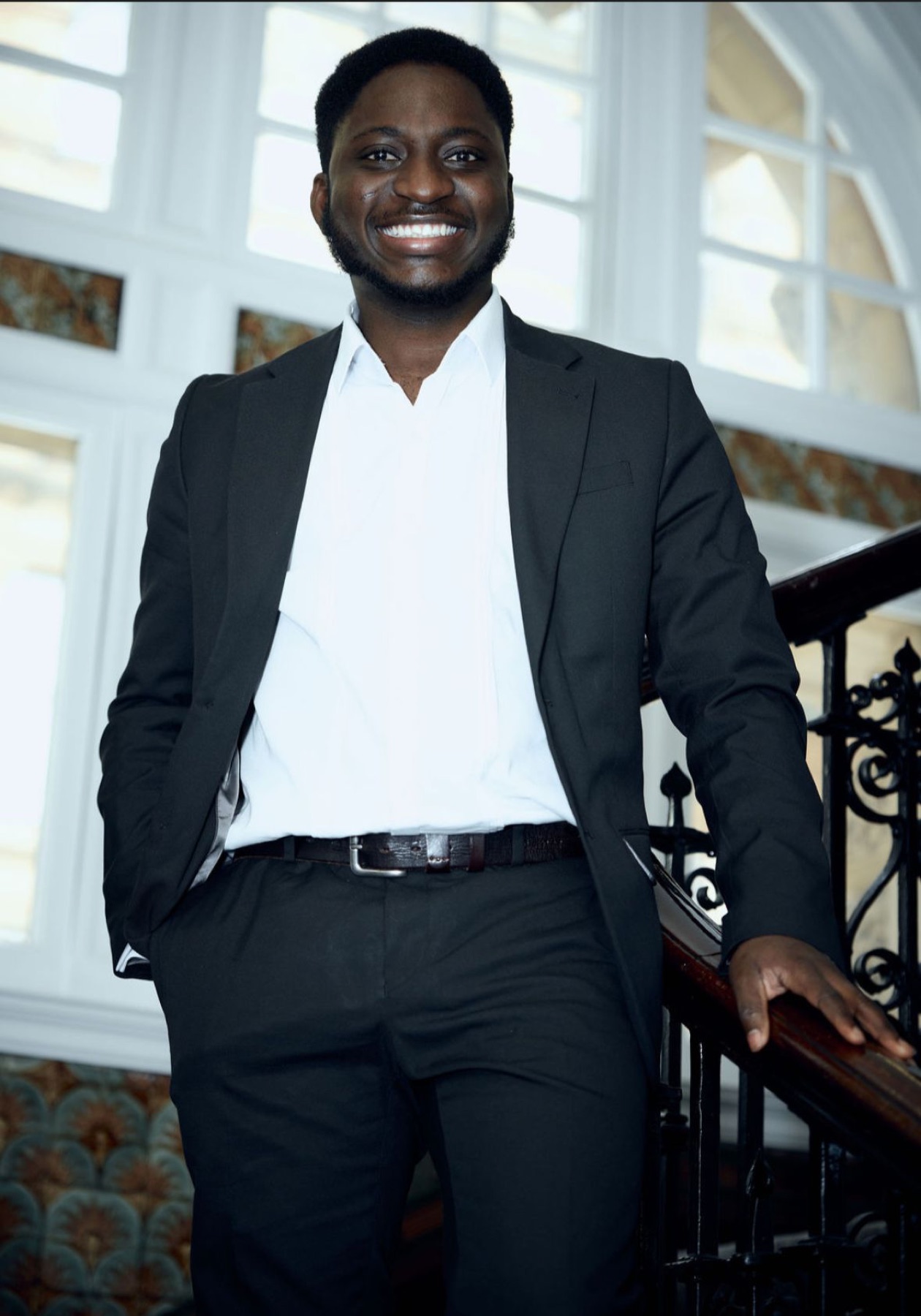 Michael Akintayo in a dark suit on a staircase, smiling